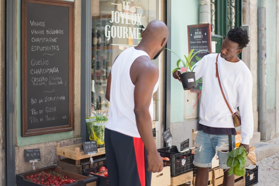 Dois homens conversam em um mercado de rua em Lisboa, Portugal, examinando produtos frescos.